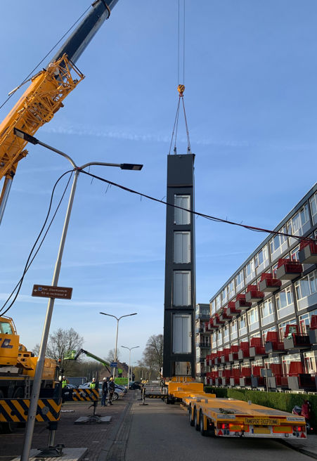Prefabricated elevator module being lifted by a large crane before installation.